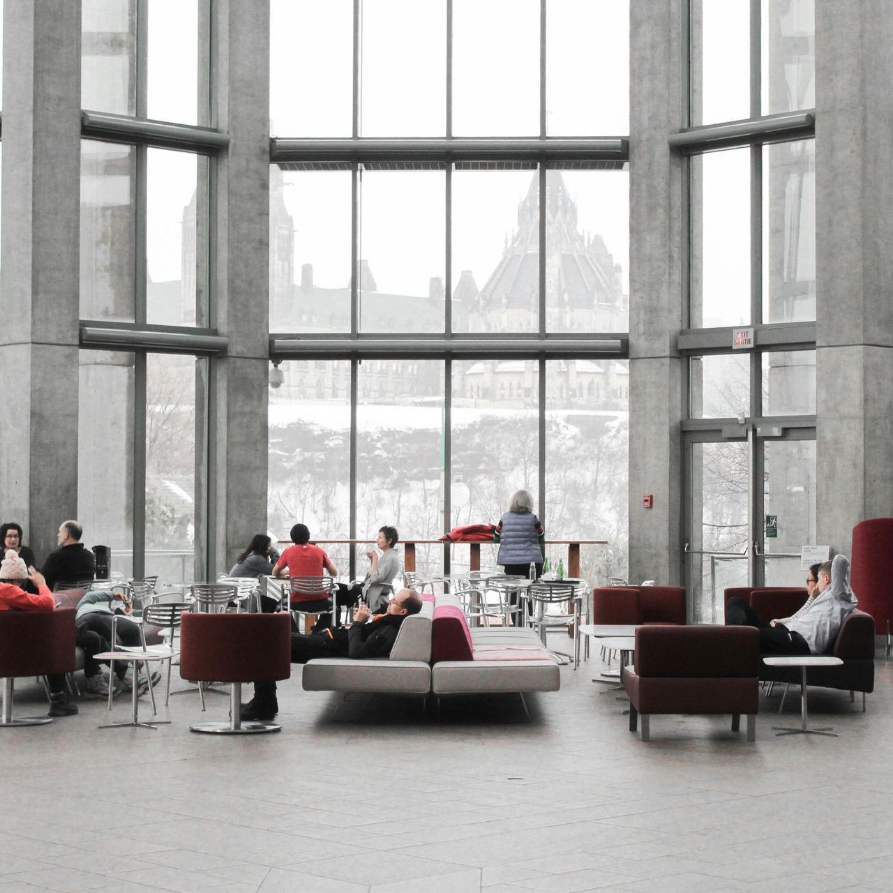 Interior of a building with large windows. People are seated on chairs and couches, with a view of a snowy landscape.