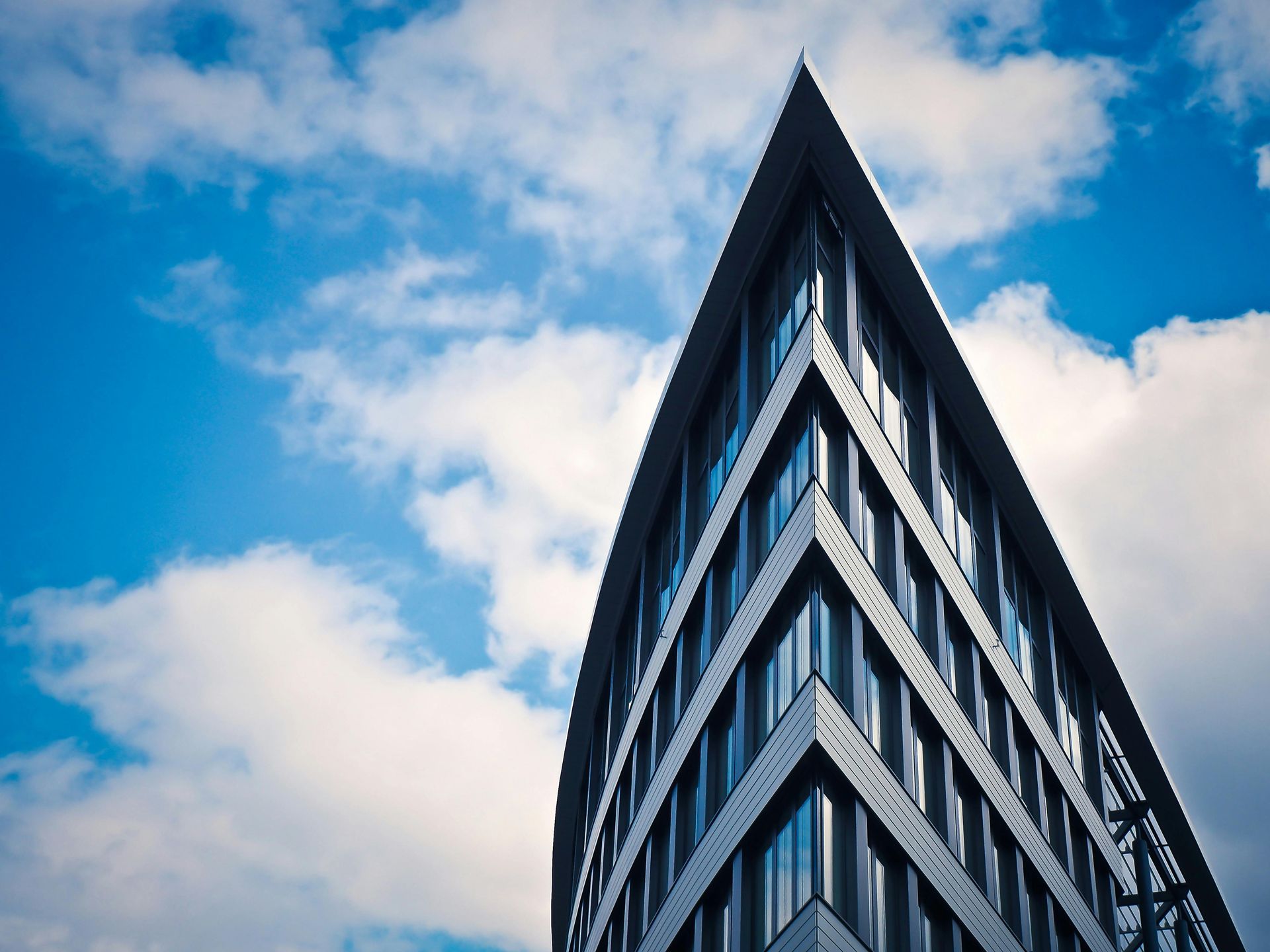 Triangular modern building against a bright blue sky with fluffy white clouds.