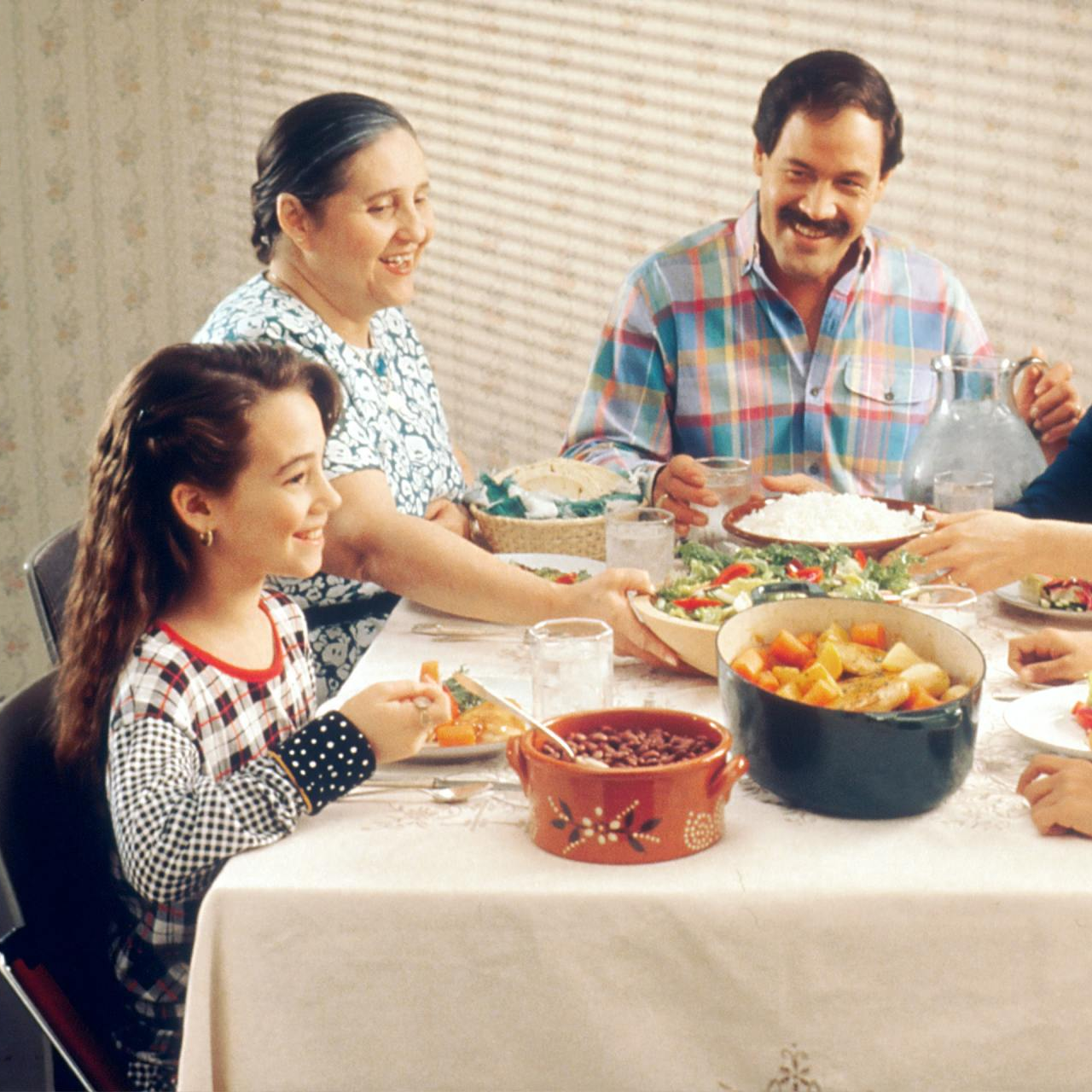 Family smiling at dinner table with food, including a girl eating.