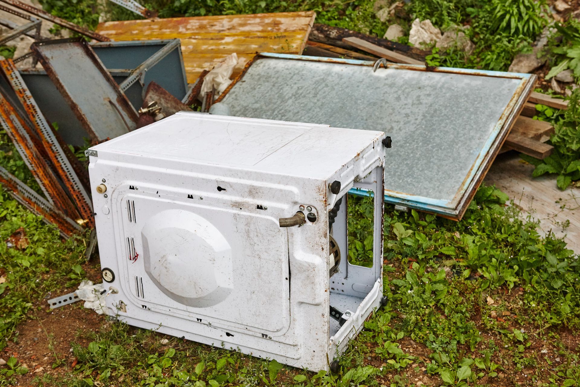 A white washing machine is sitting on top of a pile of scrap metal.
