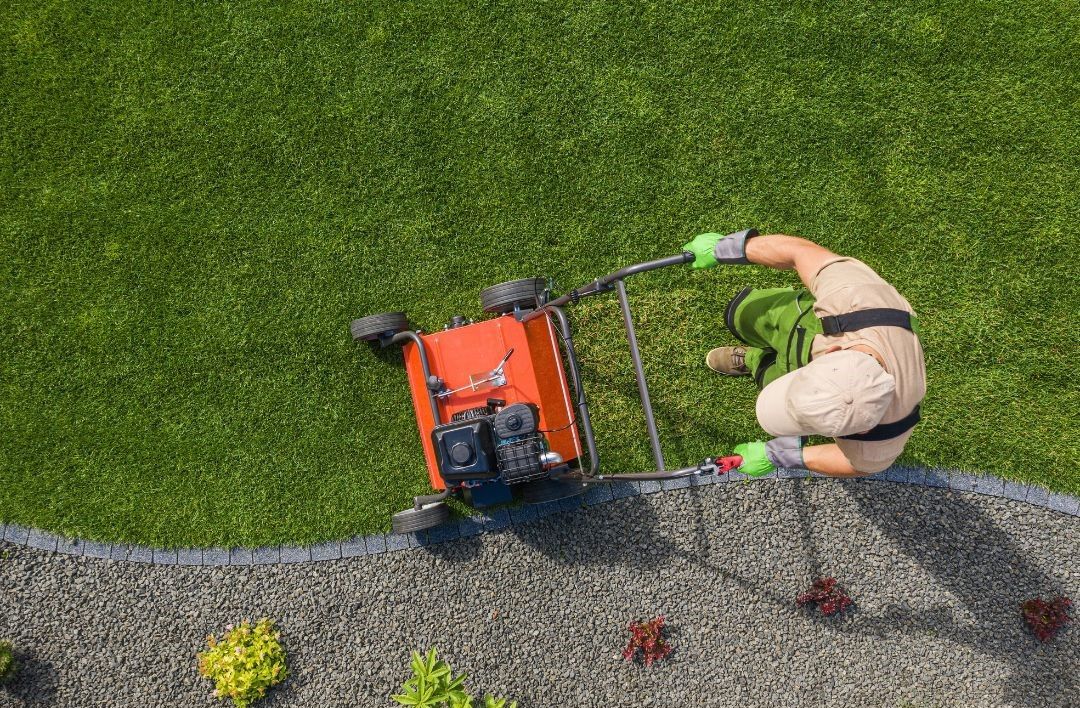An aerial view of a man using a lawn mower on a lush green lawn.