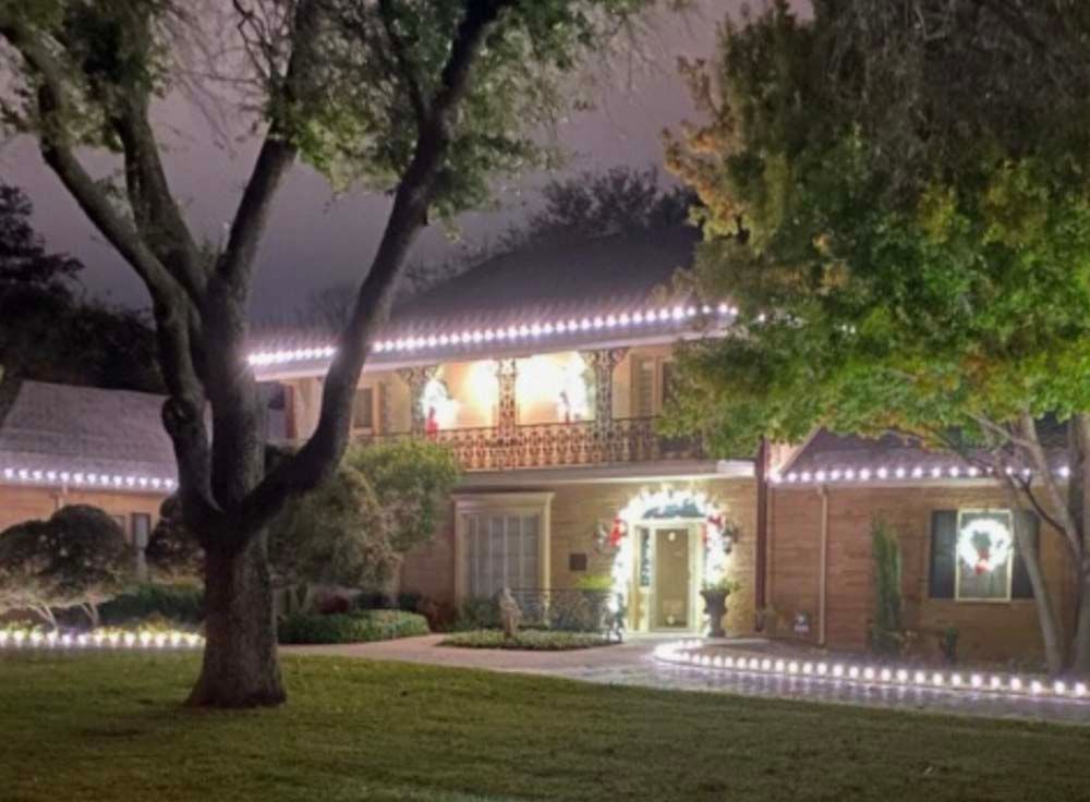 String of lit, speckled, teardrop-shaped Christmas lights clipped to a dark roof edge, glowing against a dark background.