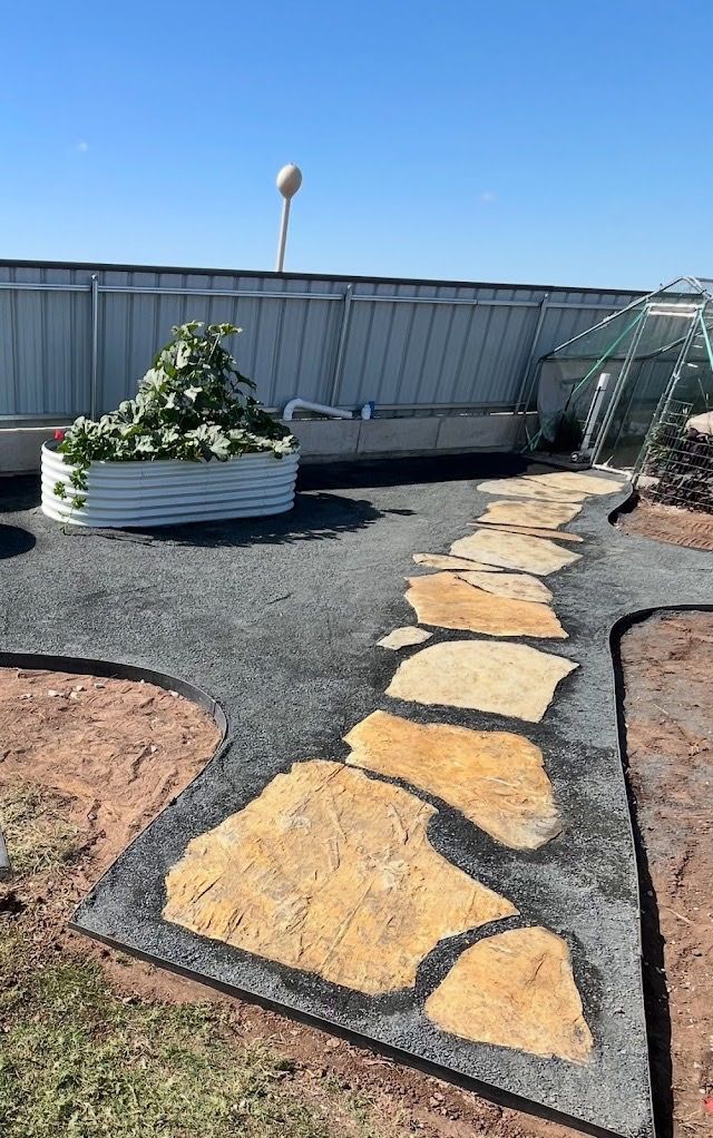 Flagstone path through a gravel garden bed, with a metal raised garden and a greenhouse in the background.