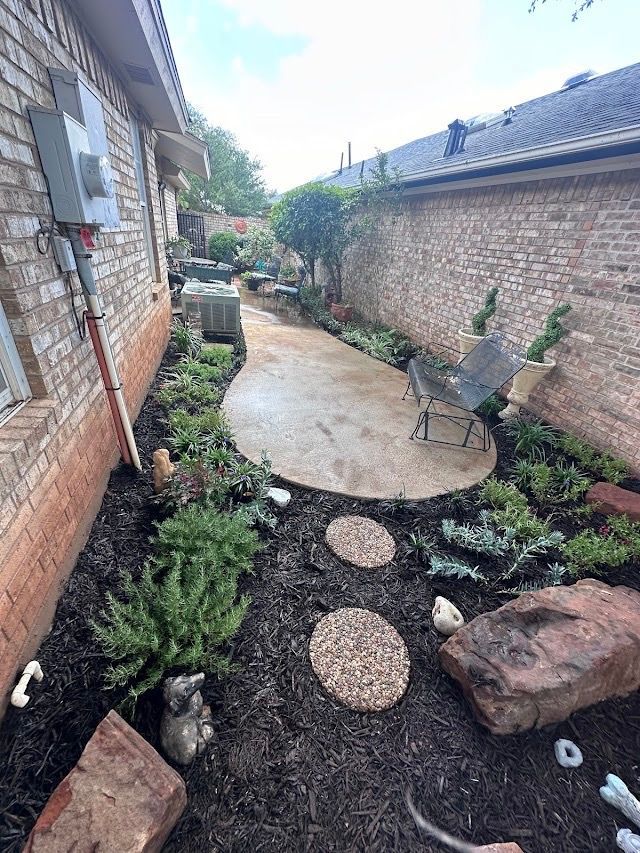 Narrow backyard with a concrete patio, landscaping, and brick walls.