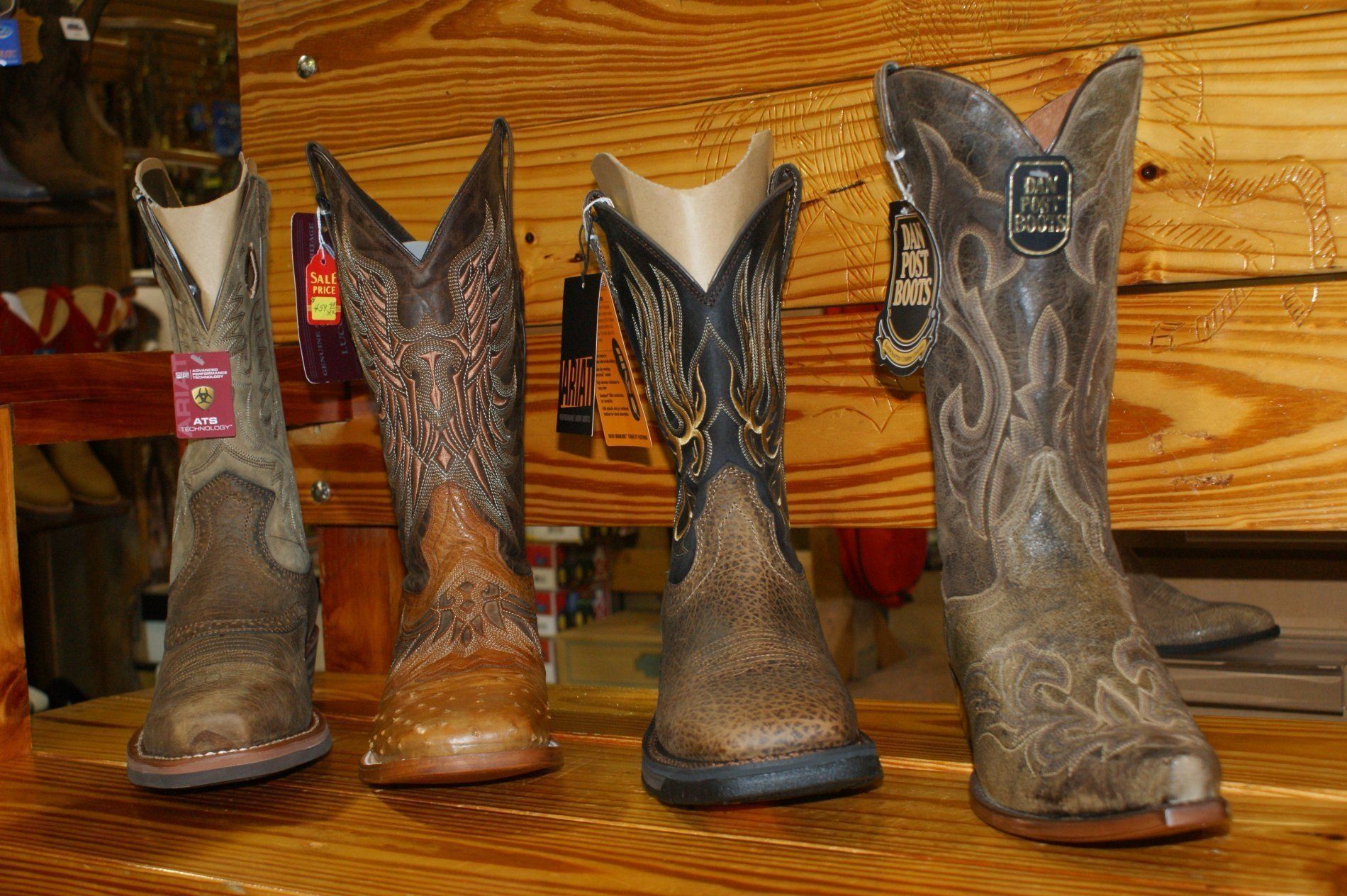 Four brown cowboy boots displayed on a wooden shelf, with intricate stitching and leather textures.