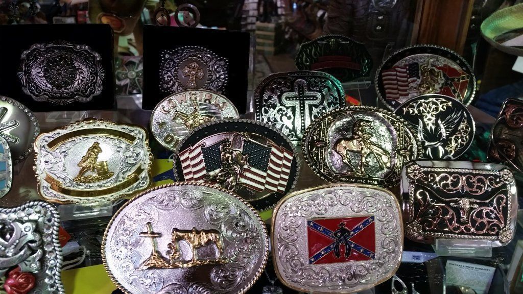 Display of ornate belt buckles with various designs, including an American flag and a Confederate flag.