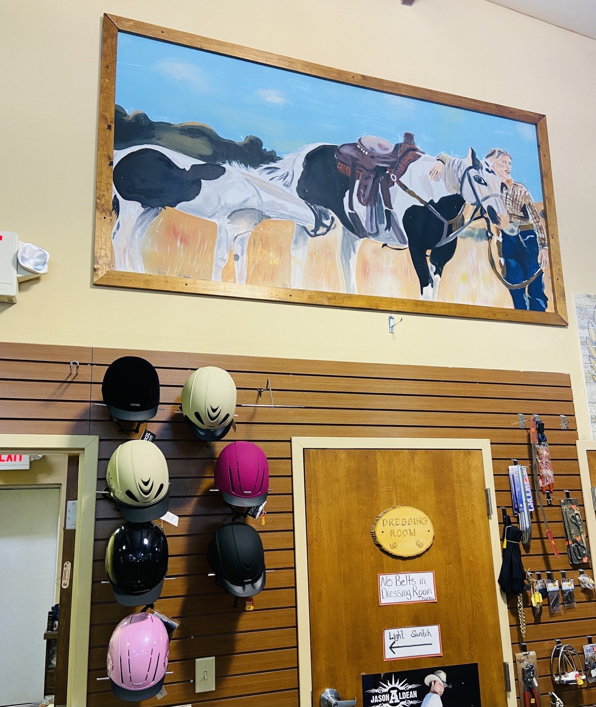 Equestrian store interior with a painting of horses above helmet display.