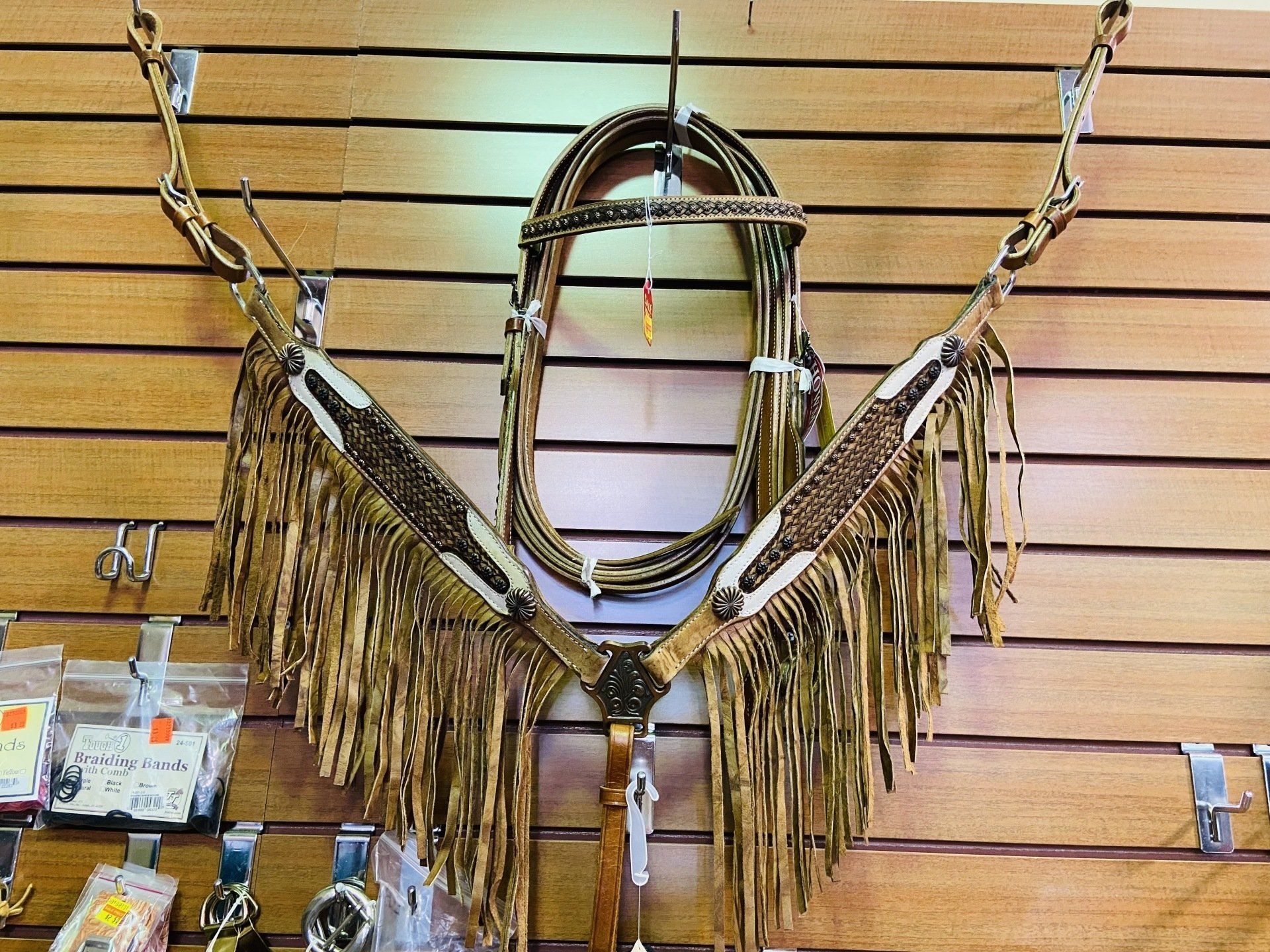 Horse tack set, featuring a bridle and breast collar, decorated with fringed elements, displayed on a wooden wall.