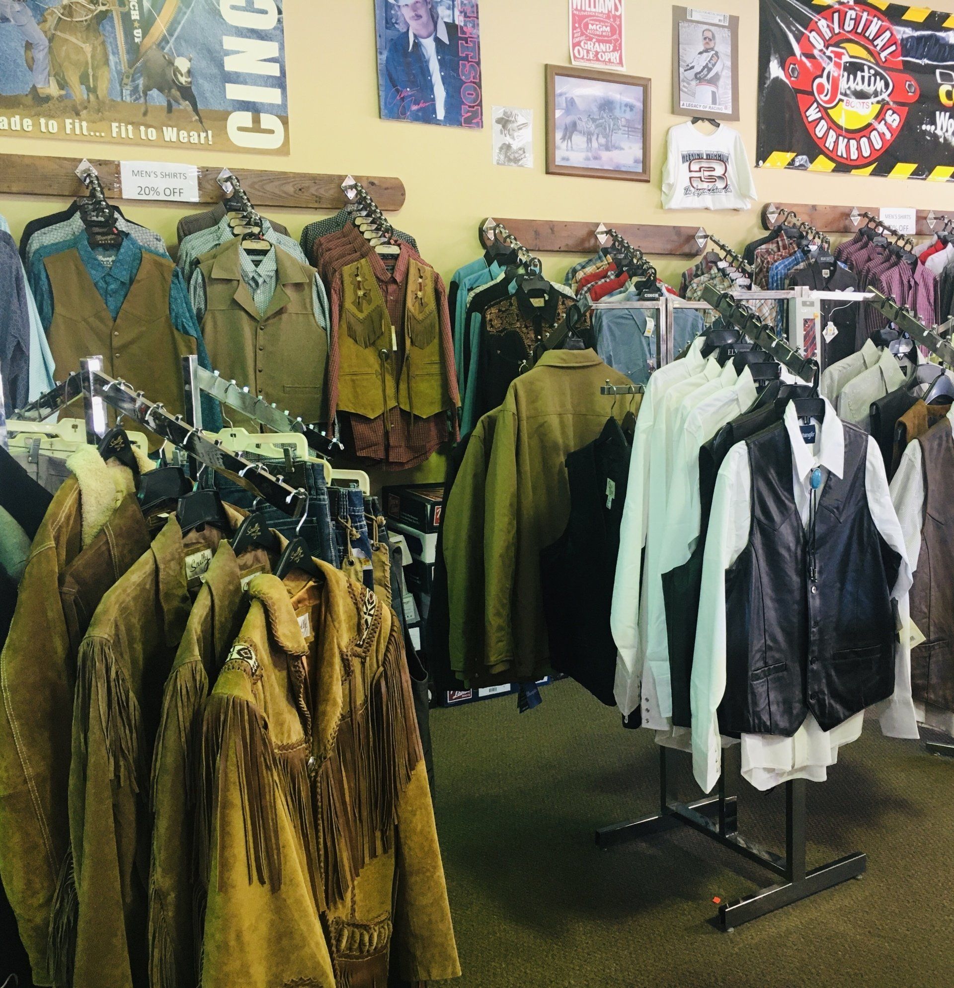 Clothing store interior with racks of jackets, shirts, and vests on display; yellow walls and posters.
