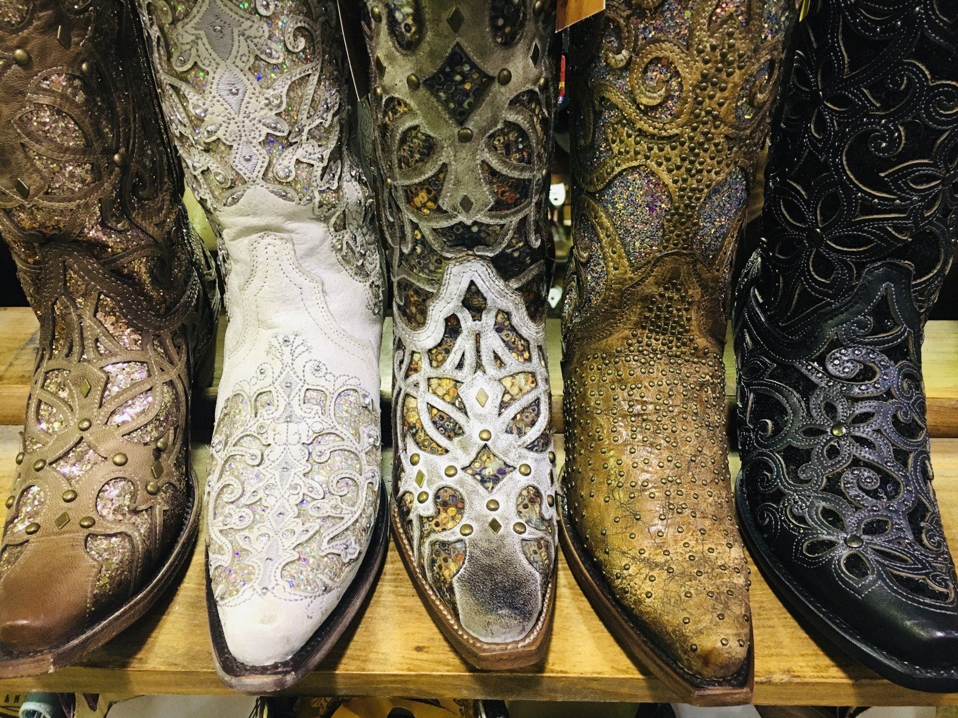 Five intricately designed cowboy boots on display. Various colors and patterns, including brown, white, and black.