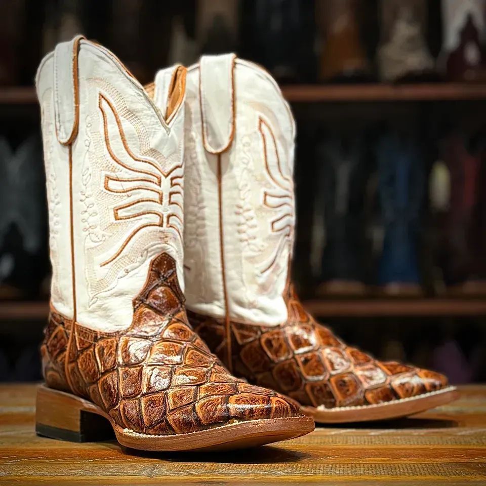 Pair of cowboy boots with white tops and brown alligator-skin vamps on a wooden surface.