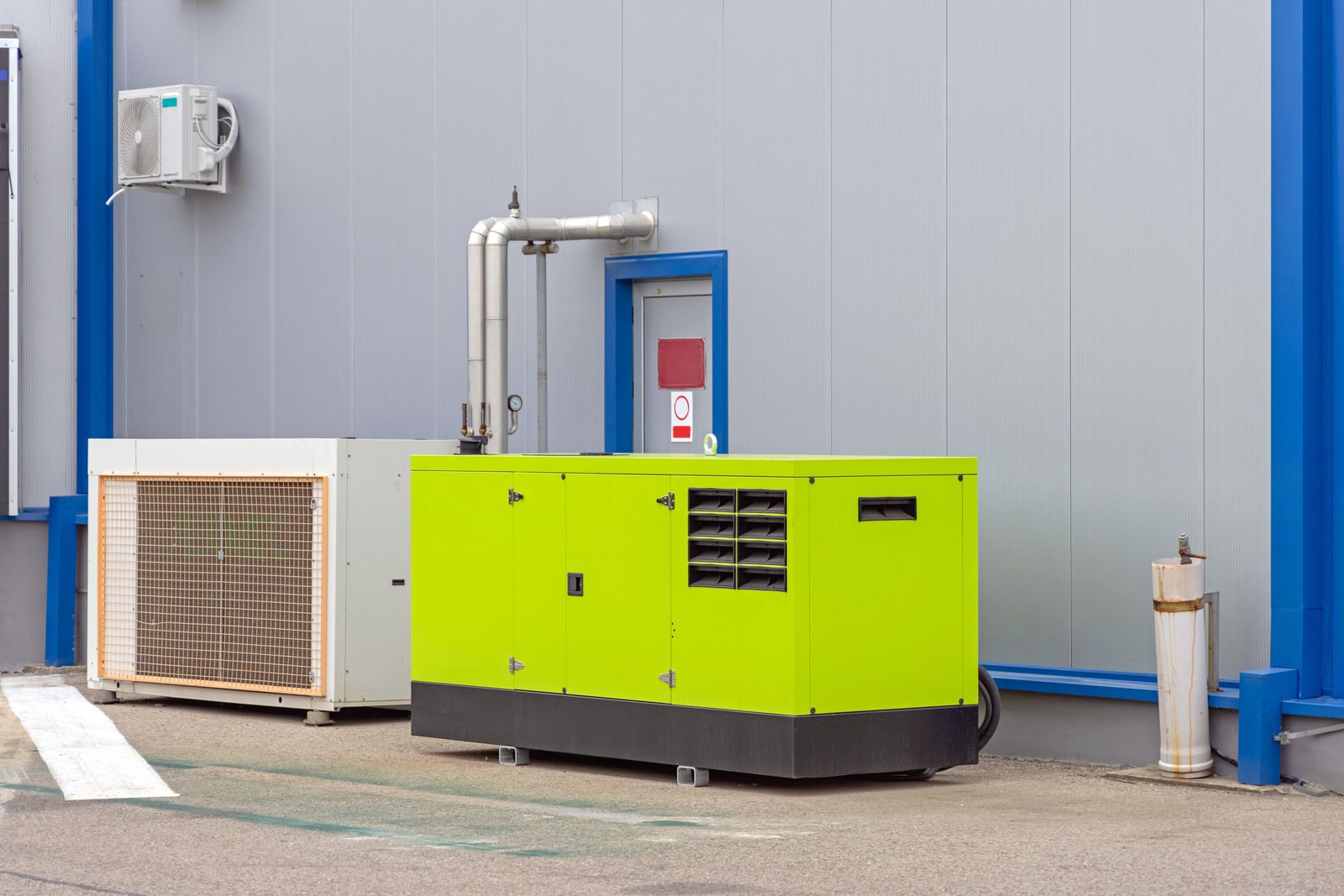 A green generator is parked in front of a building.