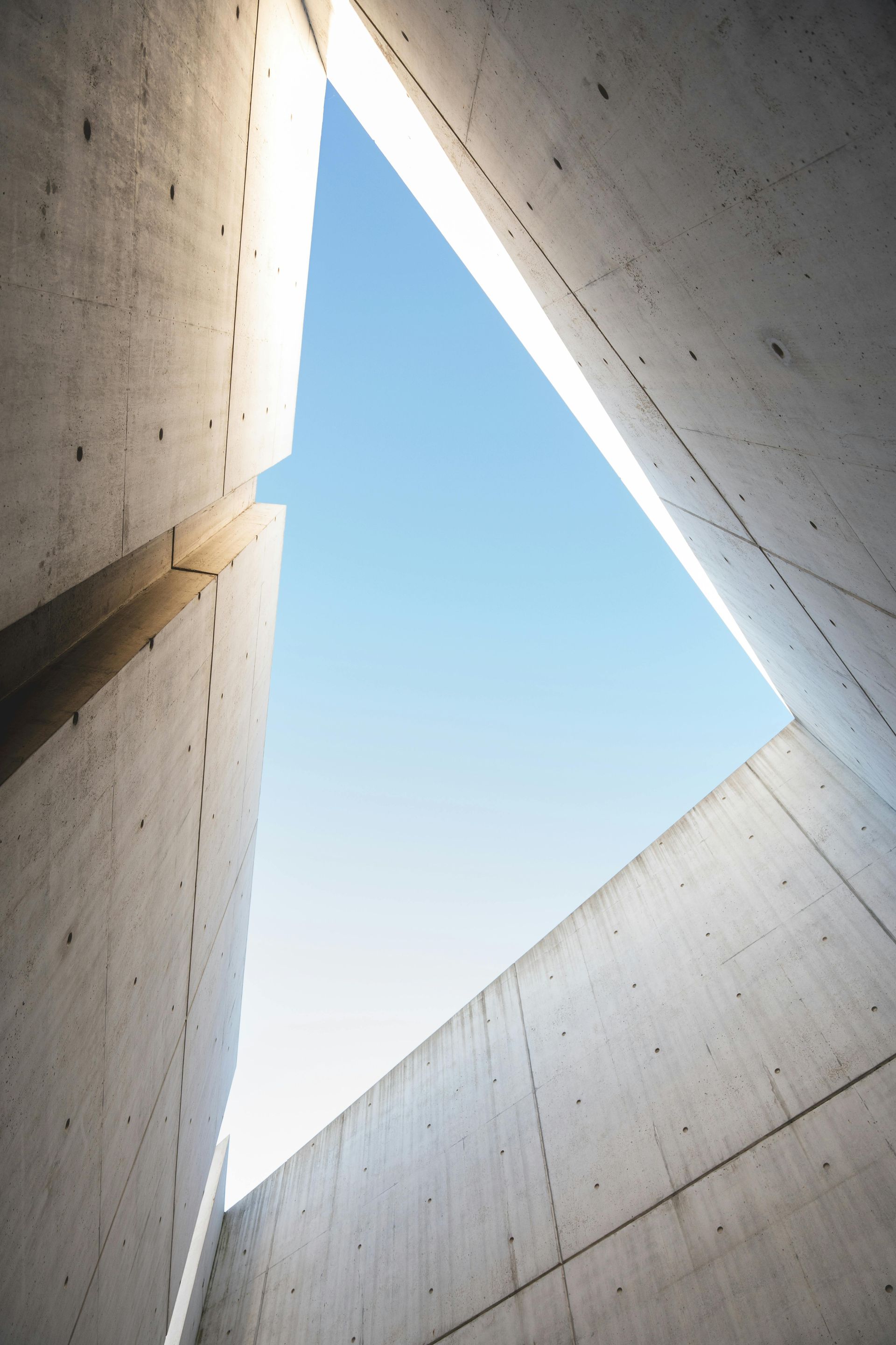 Concrete walls frame a triangular opening to a clear blue sky.