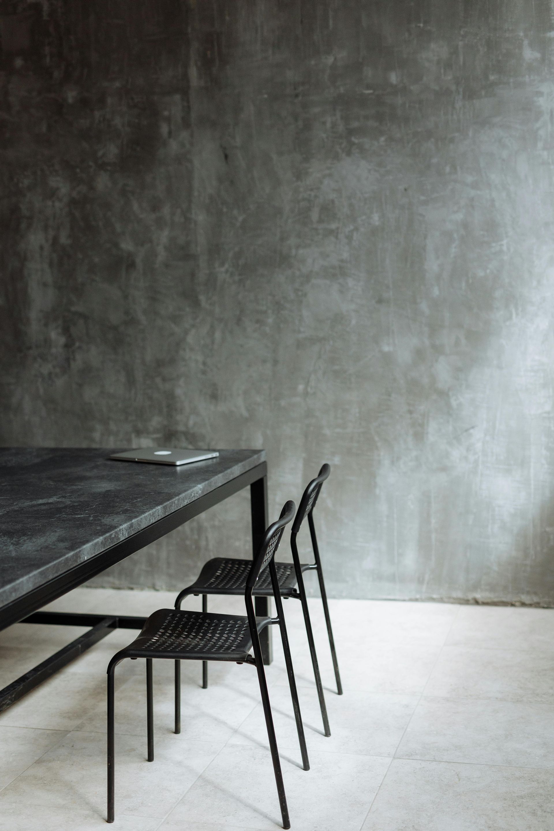 Black table and chairs against a textured gray wall and light floor.