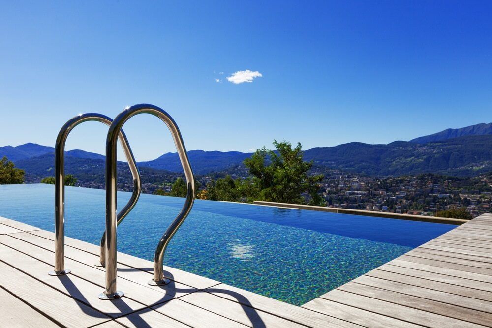 Swimming Pool With Ladder Overlooking a City and Mountains Under a Blue Sky — Creative Pools and Spas in Mount Martha, VIC