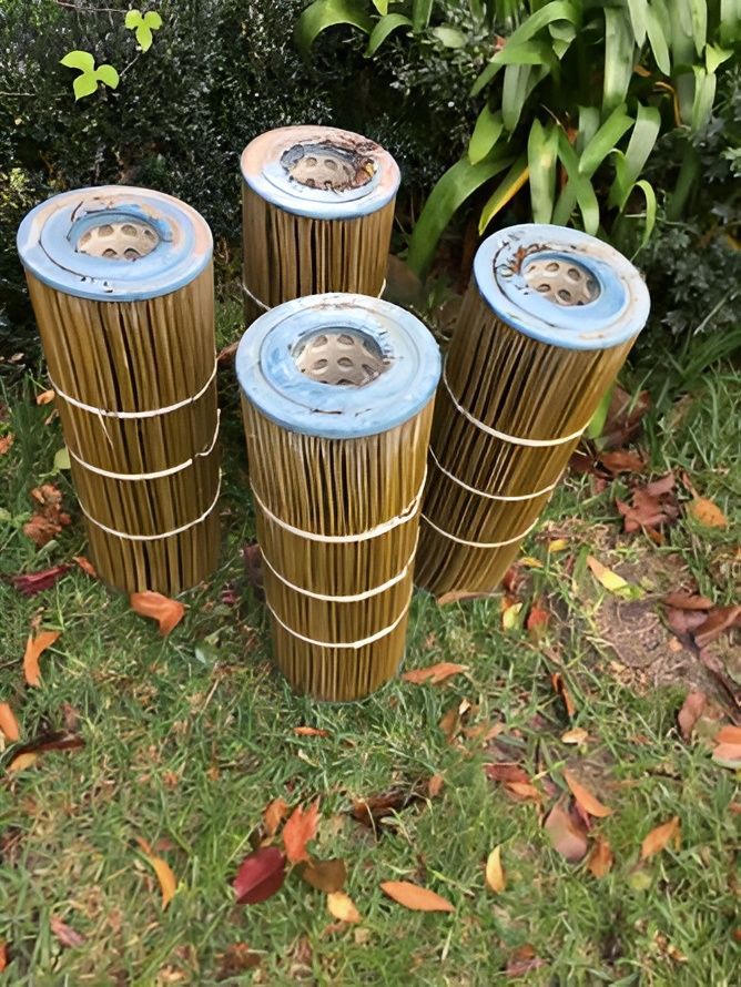 Four Used Cylindrical Pool Filter Cartridges on Grass With Autumn Leaves — Creative Pools and Spas in Rosebud, VIC