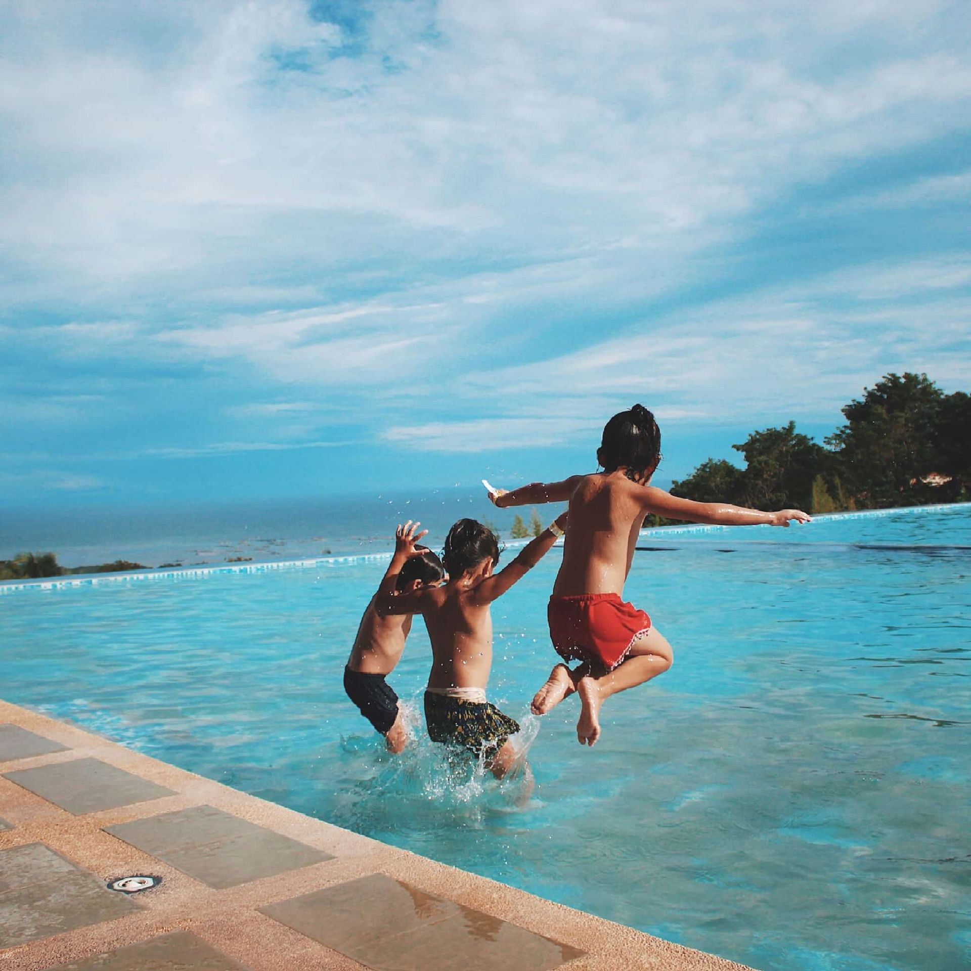 Three Young Boys Jumping Into a Blue Pool on a Sunny Day — Creative Pools and Spas in Mornington, VIC