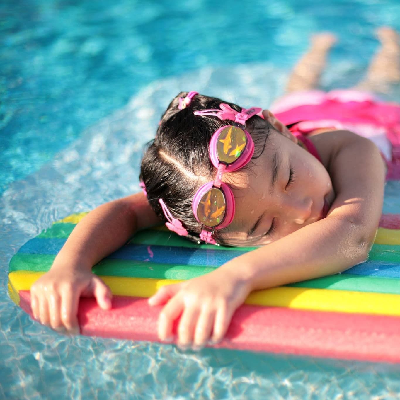 Young Girl With Pink Goggles Rests Face Down on a Rainbow Pool Float — Creative Pools and Spas in Mornington, VIC