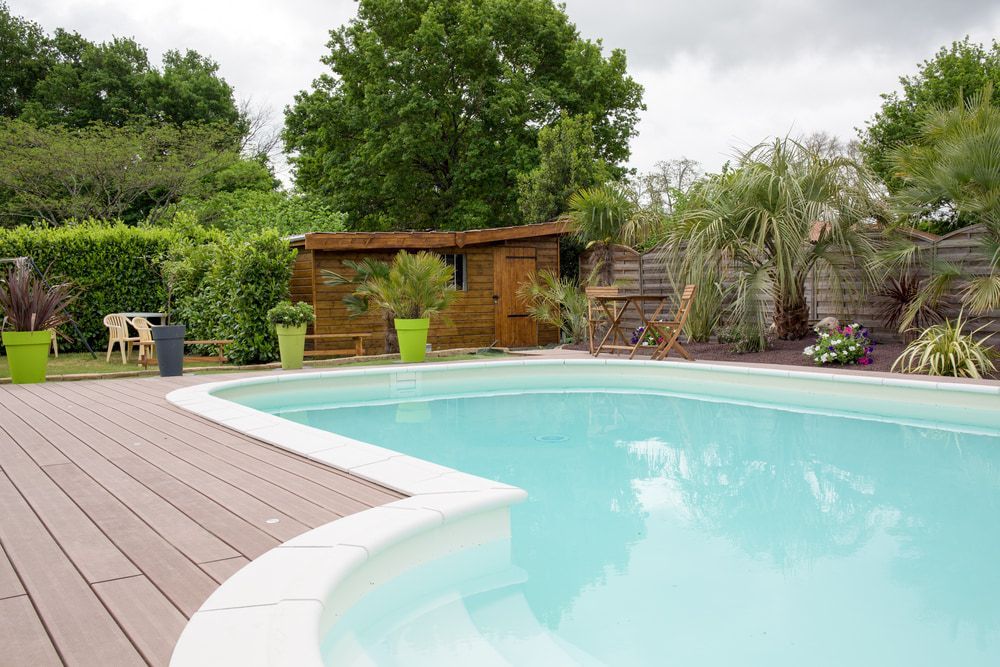 Swimming Pool With Wooden Deck, Surrounded by Lush Greenery and a Shed — Creative Pools and Spas in Mornington, VIC