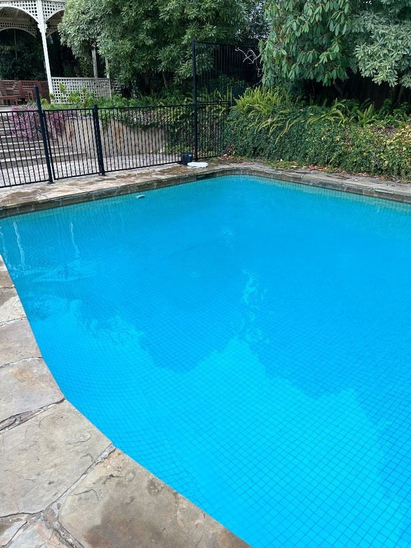 Pool With Blue Water, Surrounded by Stone Tiles and a Black Fence — Creative Pools and Spas in Mornington, VIC
