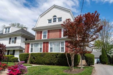 Wagner Apartments-Ardmore is a three-story brick house with white gabled roof, red shutters, and a mature tree with red leaves.