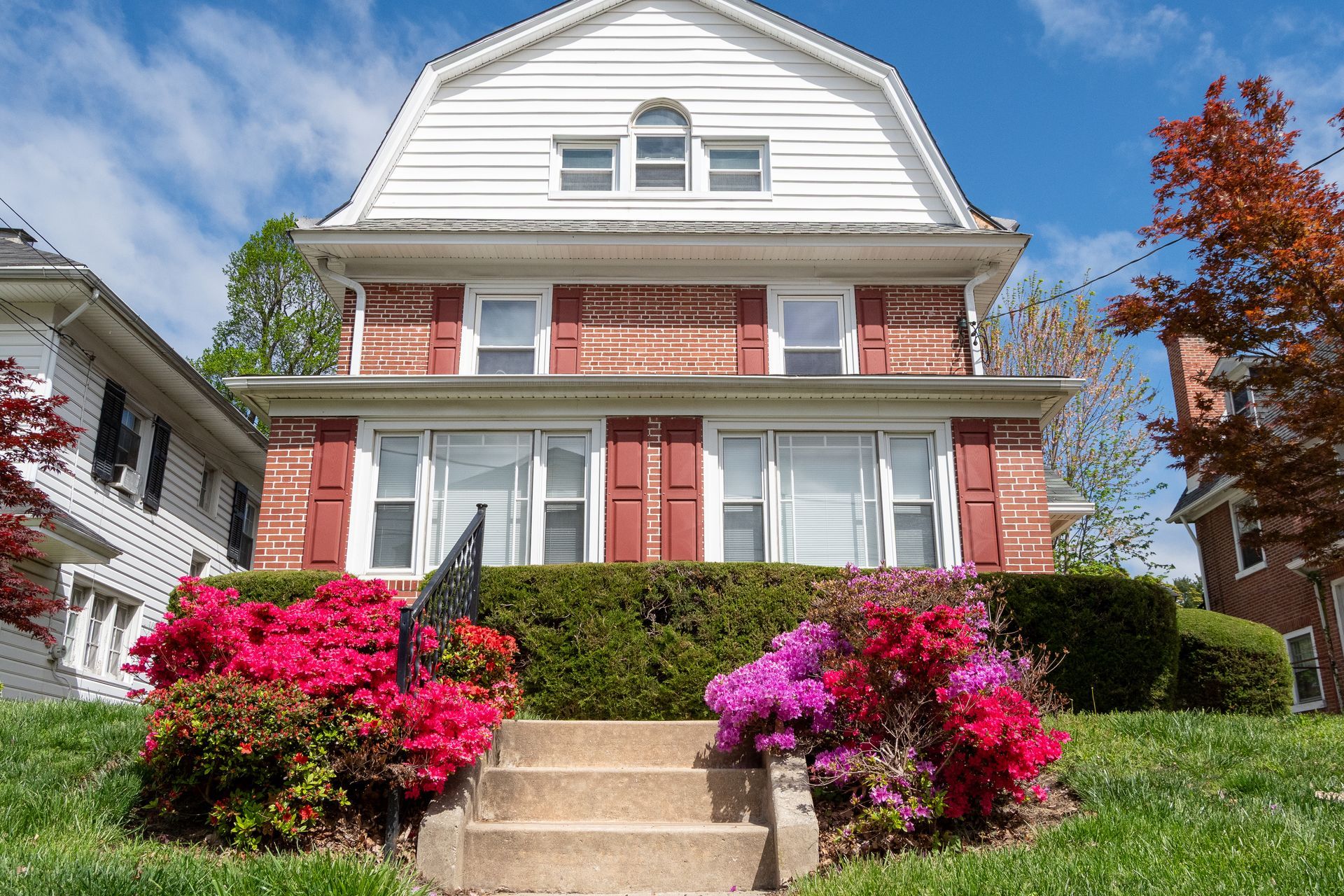A large brick house with red shutters on the windows and white siding on the third floor.
