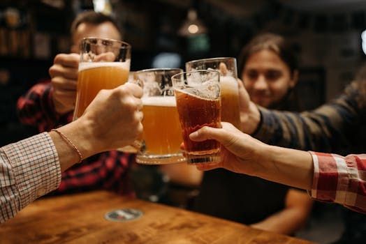 People at a bar clink beer glasses in a toast. Close-up of hands with mugs of varying amber beers.