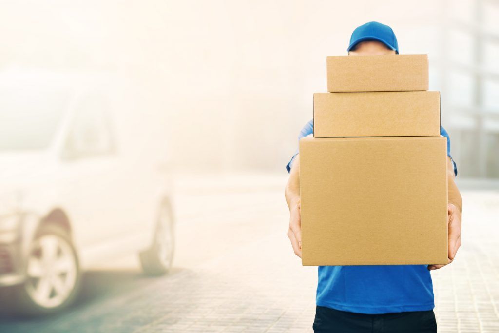 A furniture delivery man is holding a stack of cardboard boxes
