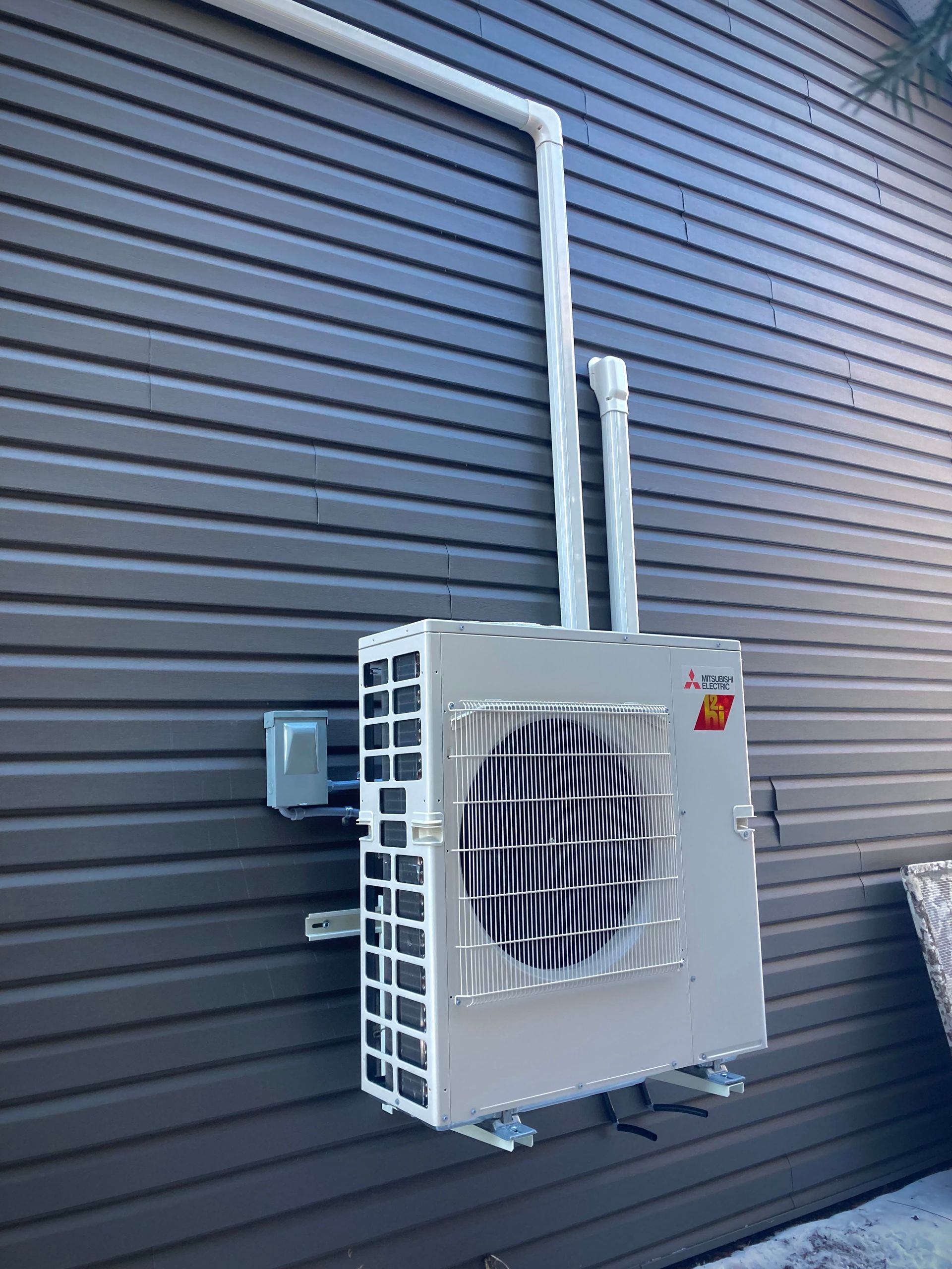 A mitsubishi air conditioner is mounted on the side of a house.