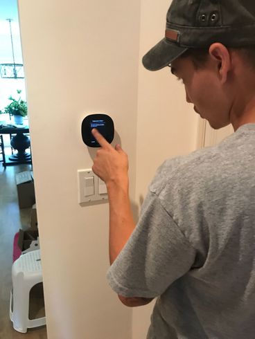 A man in a hat is using a thermostat on a wall.