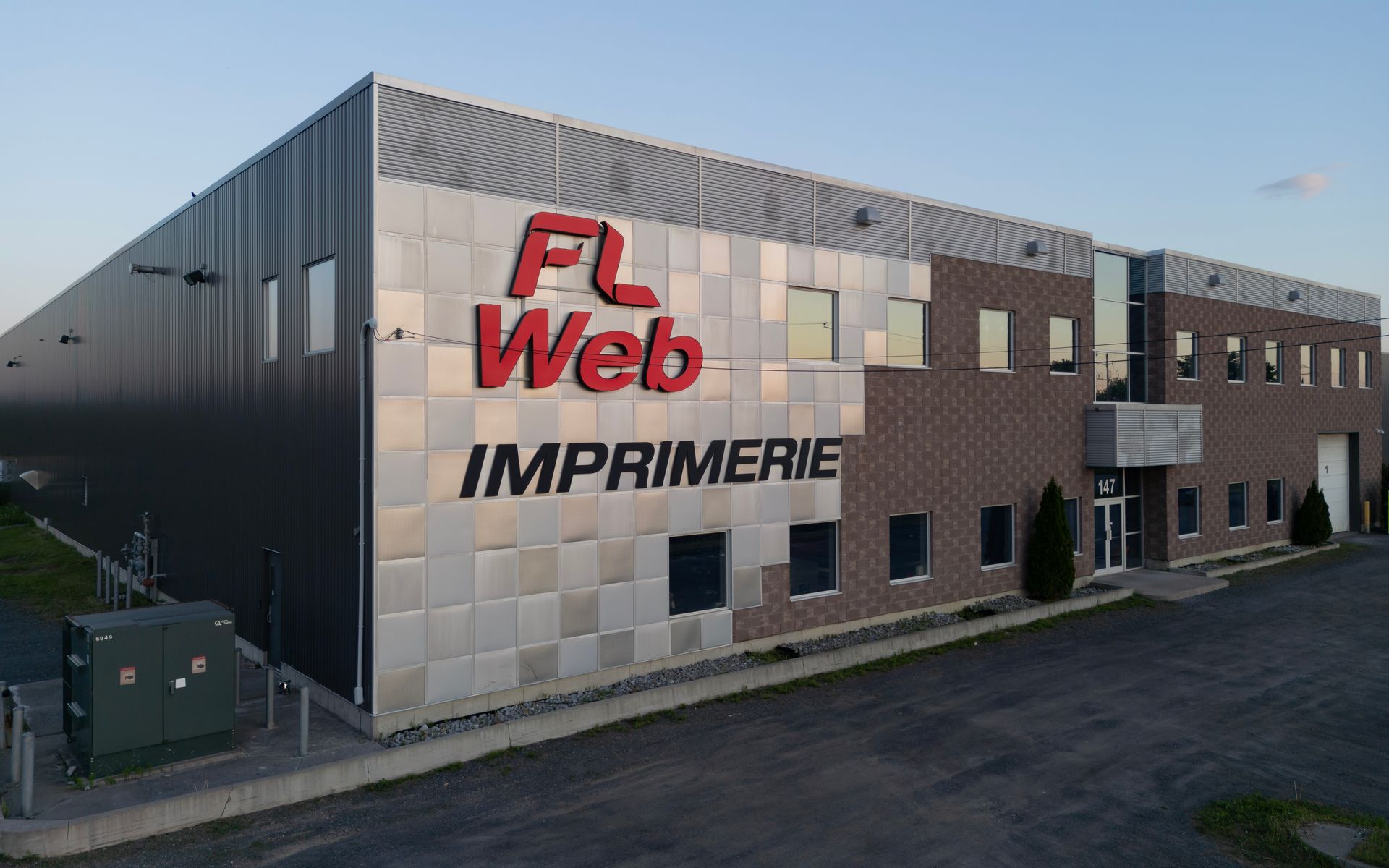 Bâtiment moderne avec une enseigne « FL Web IMPRIMERIE » rouge ; extérieur gris et marron.
