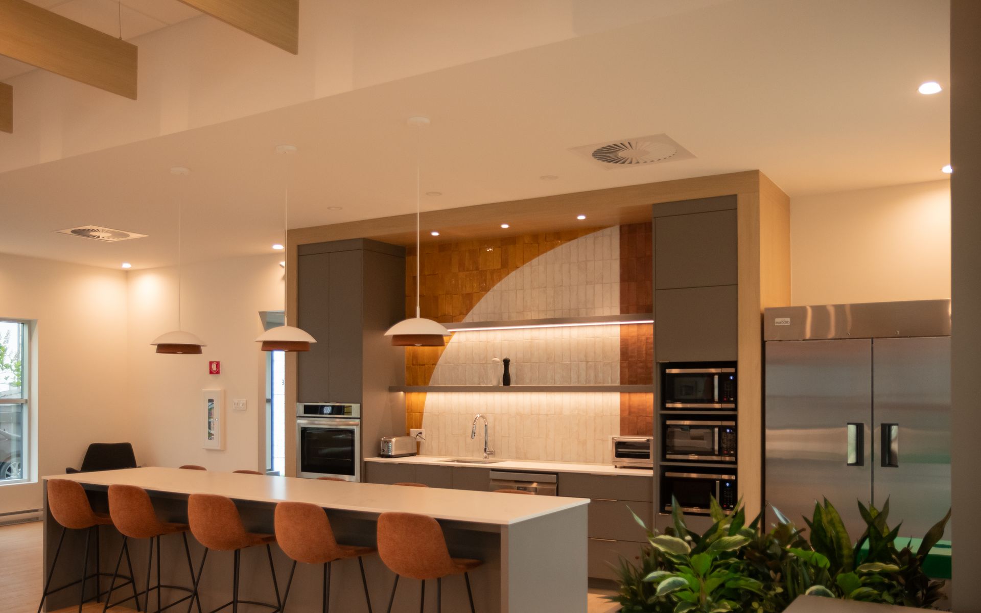 Cuisine moderne avec grand îlot central, armoires grises, appareils électroménagers en acier inoxydable et tabourets de bar orange.