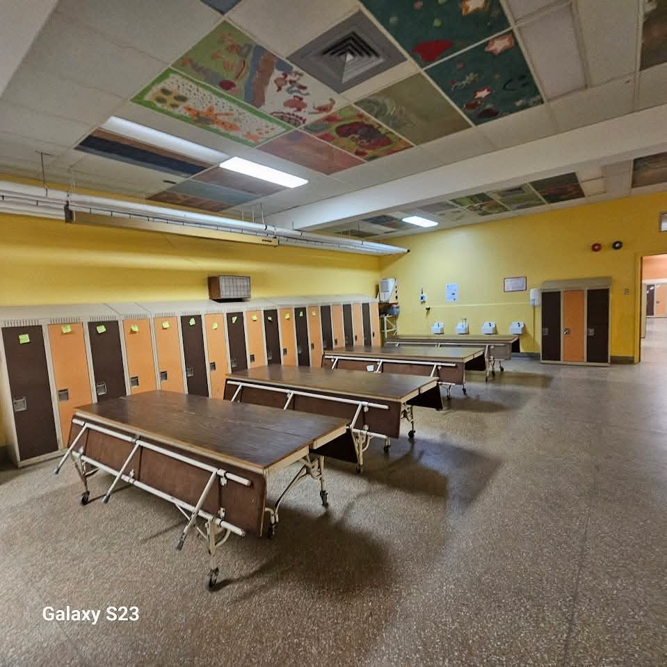 Salle de pause avec murs jaunes, casiers et tables. Plafond décoré.