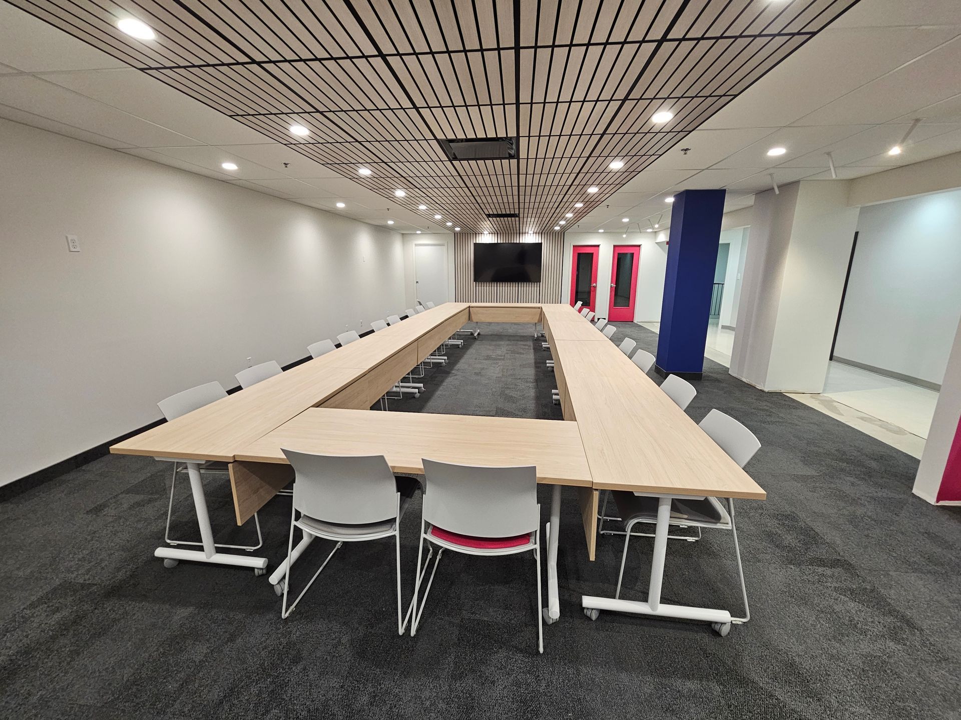 Salle de conférence avec table et chaises en forme de U, un écran et un plafond texturé.