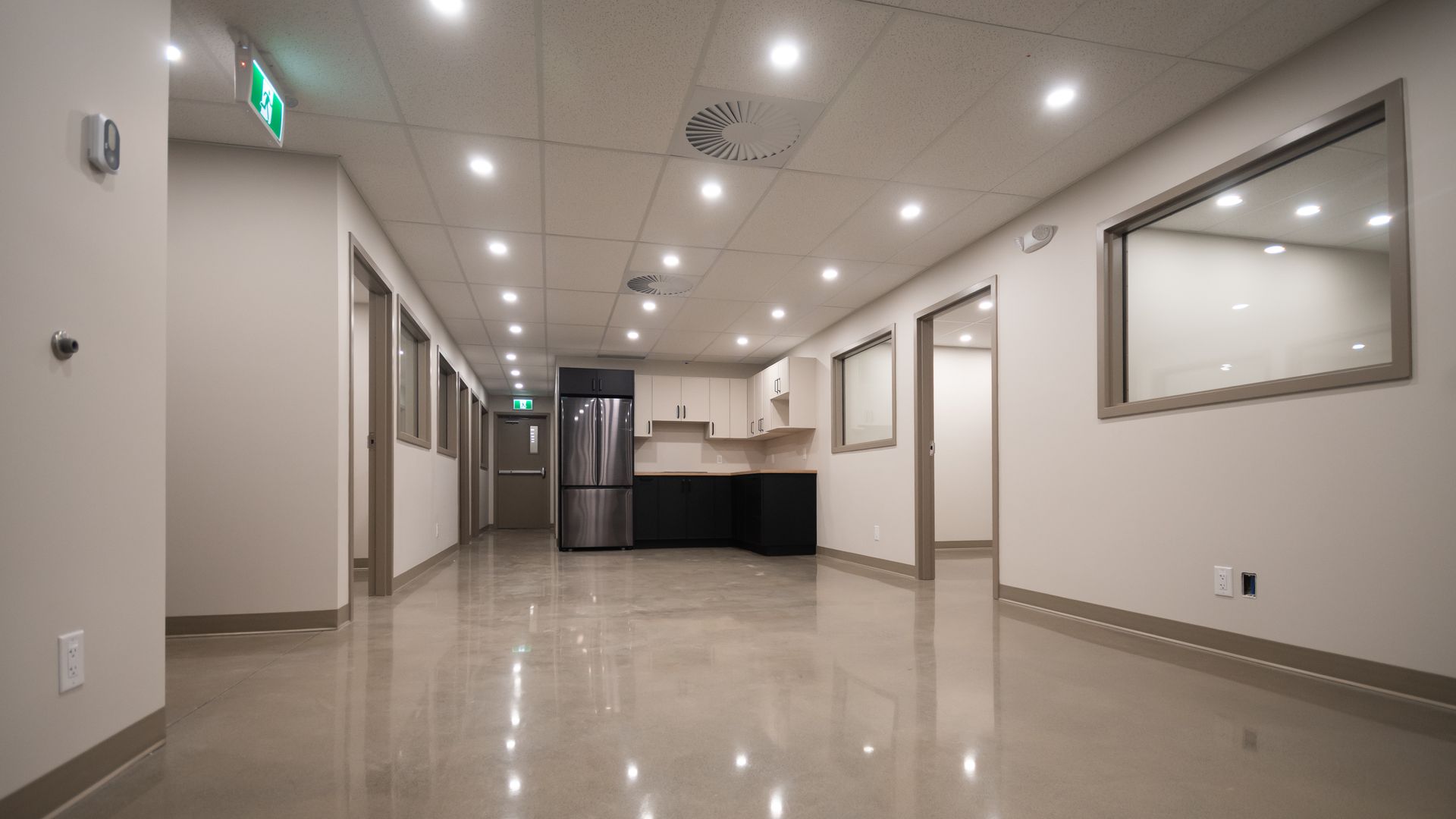 Long couloir lumineux avec éclairage encastré, réfrigérateur en acier inoxydable et petit coin cuisine.