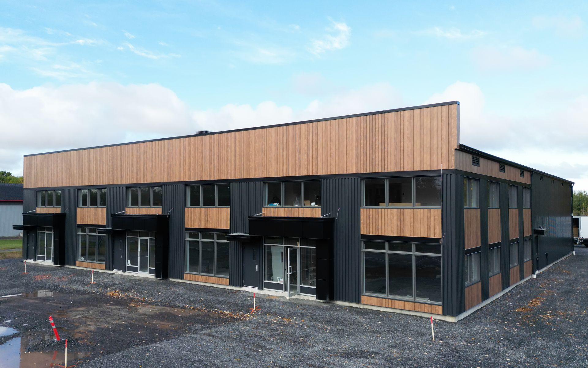 Vue extérieure d'un bâtiment moderne de deux étages avec lambris et bardage noir. Ciel nuageux.