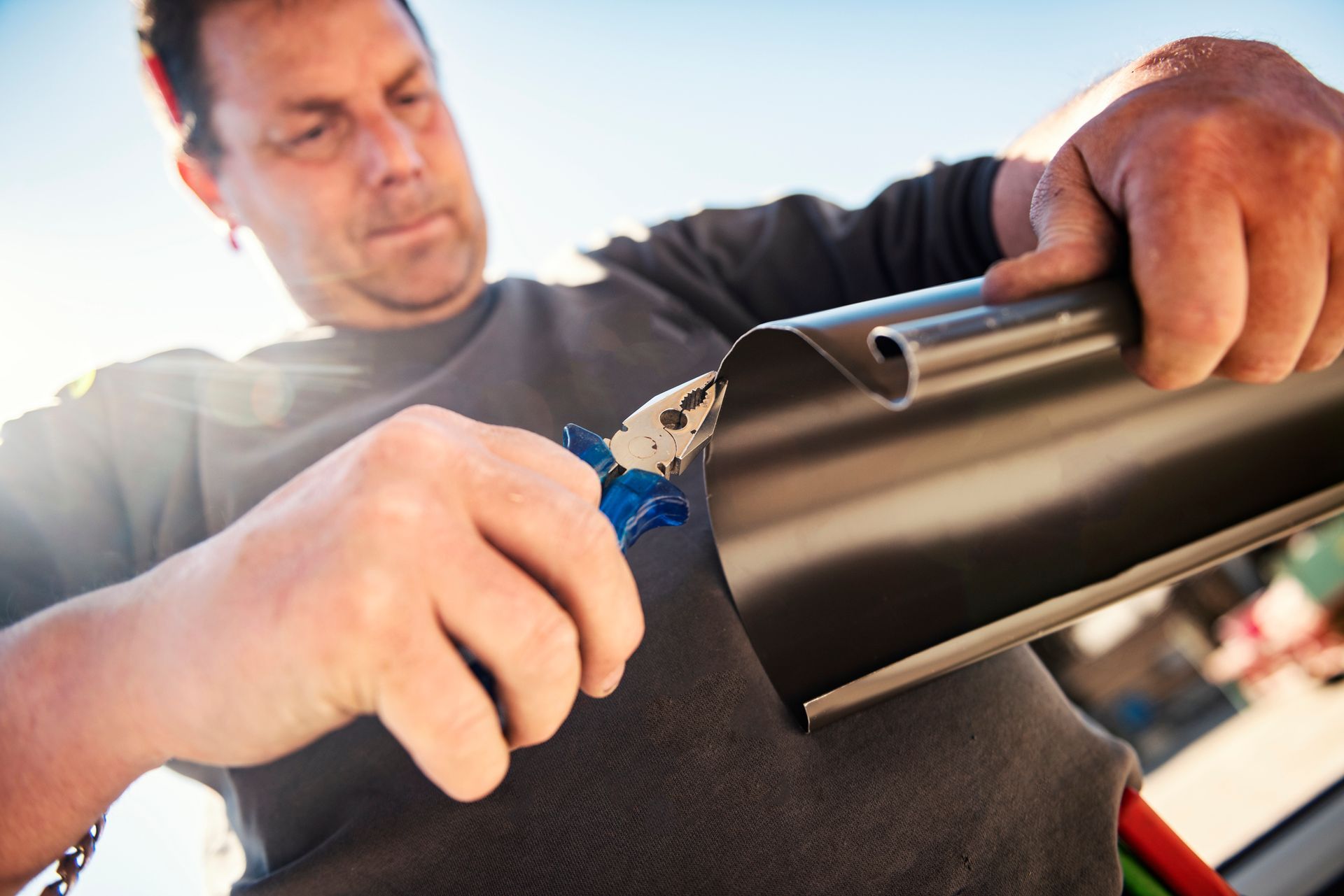 A man cutting metal with snips, illustrating a task involved in residential gutter installation. A man cutting metal with snips, illustrating a task involved in residential gutter installation.