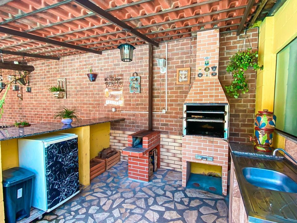 Um pátio externo rústico com paredes de tijolos, churrasqueira embutida, piso de pedra, um pequeno balcão e uma pia.