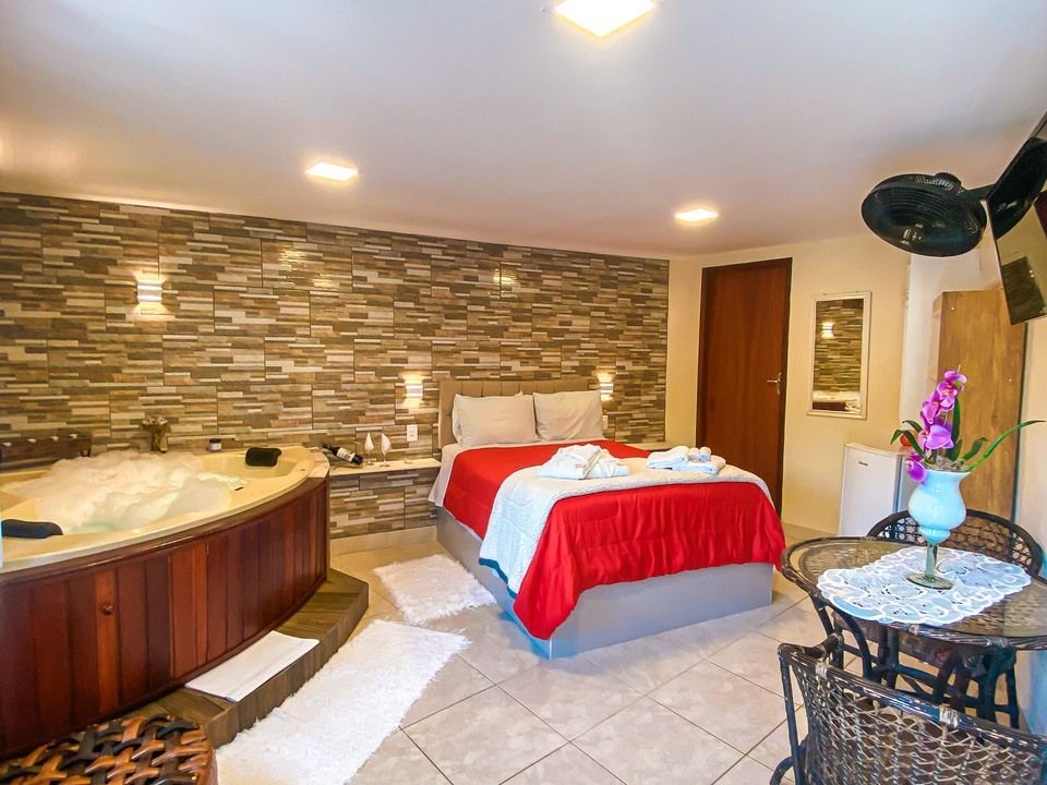 Um quarto de hotel com banheira de hidromassagem, cama com colcha vermelha e uma pequena mesa de jantar com cadeiras.