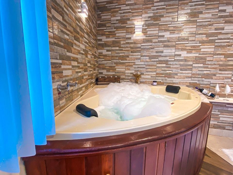 Uma banheira de canto com água cheia de espuma, painéis de madeira e paredes revestidas com azulejos de pedra em um quarto aconchegante.