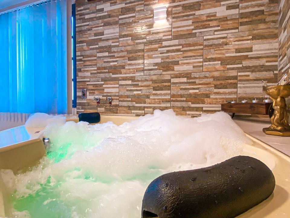 Uma banheira de hidromassagem borbulhante com iluminação subaquática verde e um encosto de cabeça preto, encostada em uma parede de pedra empilhada.