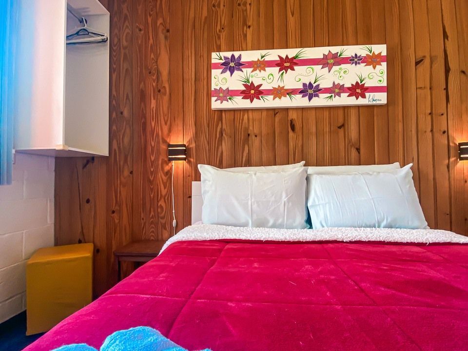 Um quarto com paredes revestidas de madeira, uma colcha rosa vibrante, dois travesseiros e uma obra de arte floral acima da cabeceira.