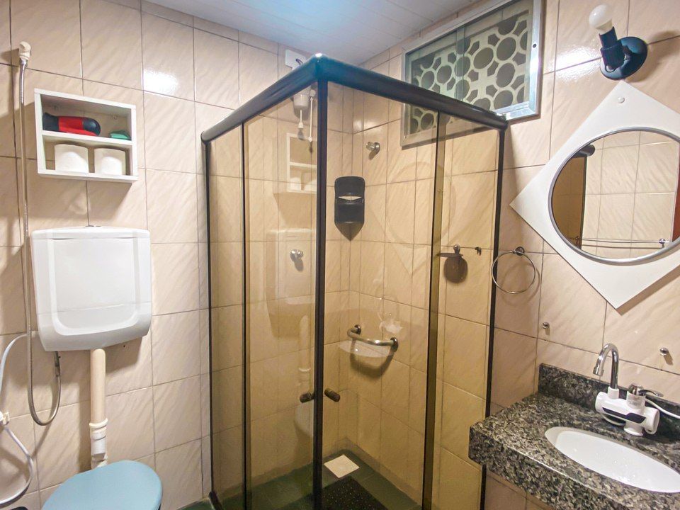 Um banheiro com vaso sanitário, box de vidro de canto para chuveiro, pia com bancada e espelho decorativo em formato de diamante.