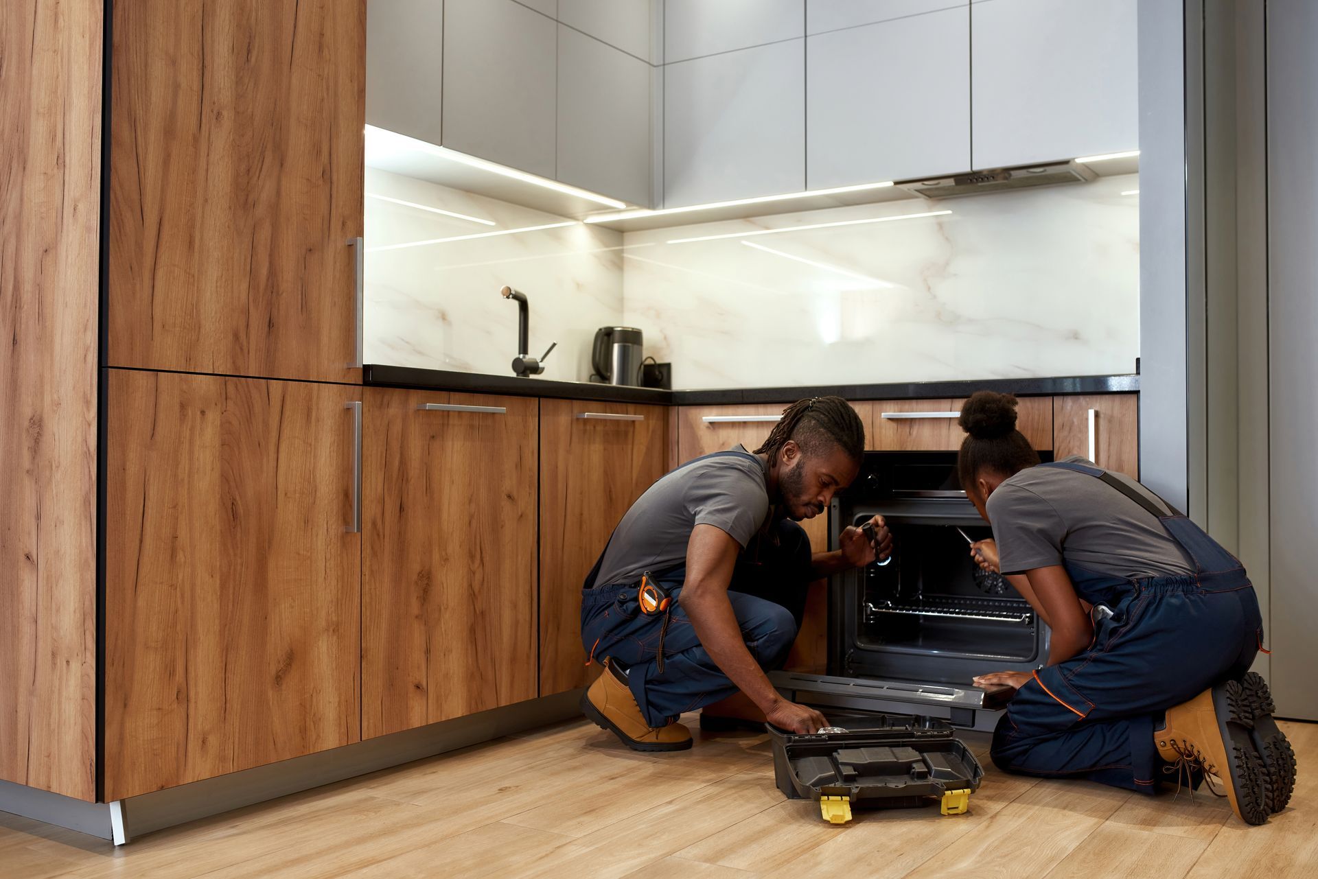 Two men are working on an oven in a kitchen.