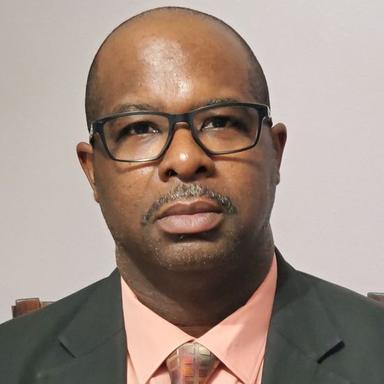 A man wearing glasses and a suit looks at the camera