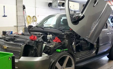 Gray SUV with gullwing doors open in a garage, engine bay exposed.