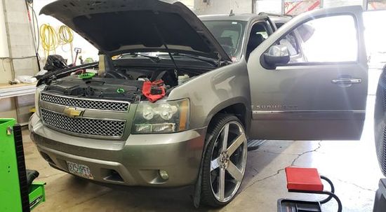 Gray Chevrolet SUV with hood open and door ajar, in a repair shop.