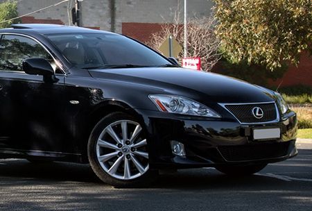 Black Lexus car parked on a street with trees in the background.