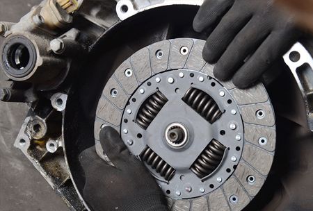 Hands in black gloves installing a clutch disc in a car transmission.