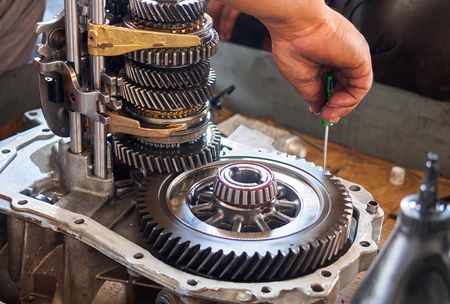 Mechanic working on car transmission, using a screwdriver, showing gears and bearings.